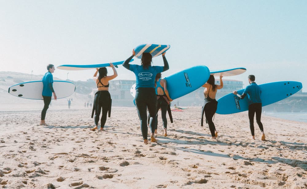 Gruppe mit Surfbrettern geht am sonnigen Strand zum Meer