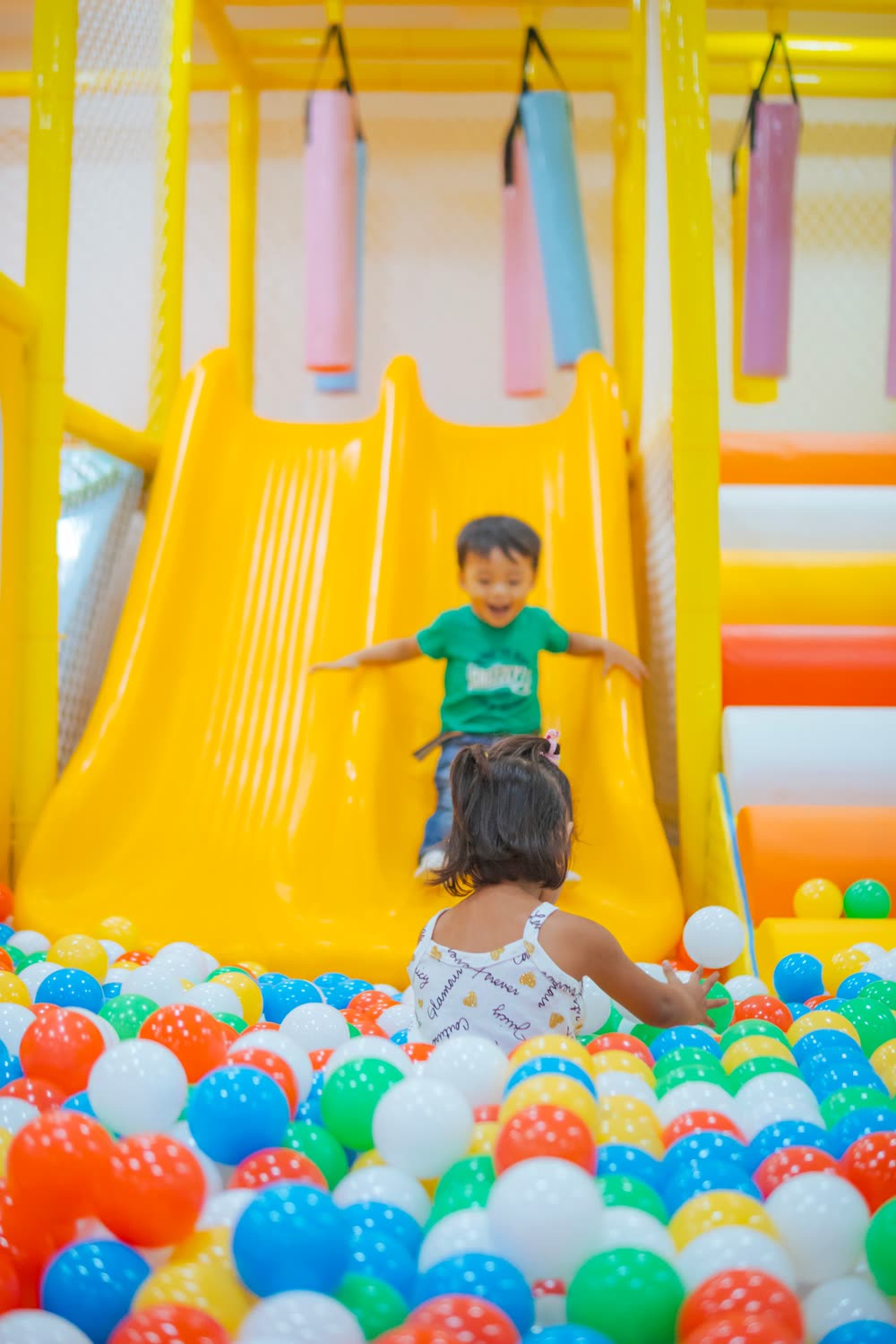 Kinder auf einer gelben Rutsche über einem bunten Bällebad